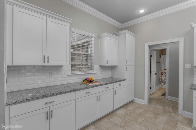 kitchen featuring ornamental molding, decorative backsplash, light stone countertops, baseboards, and white cabinets