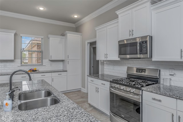 kitchen featuring crown molding, decorative backsplash, white cabinetry, a sink, and appliances with stainless steel finishes
