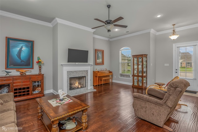 living area with crown molding, a ceiling fan, a warm lit fireplace, and wood finished floors