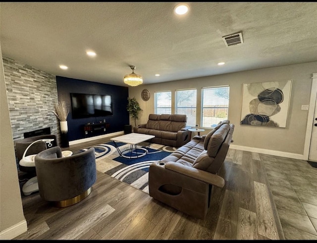 living room with baseboards, a stone fireplace, a textured ceiling, and wood finished floors