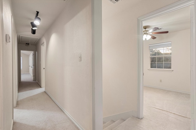 hall featuring baseboards, attic access, and carpet flooring