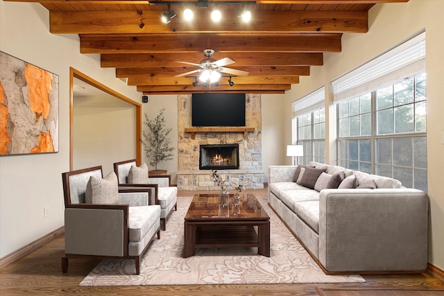 living area with beam ceiling, a stone fireplace, a ceiling fan, wooden ceiling, and wood finished floors