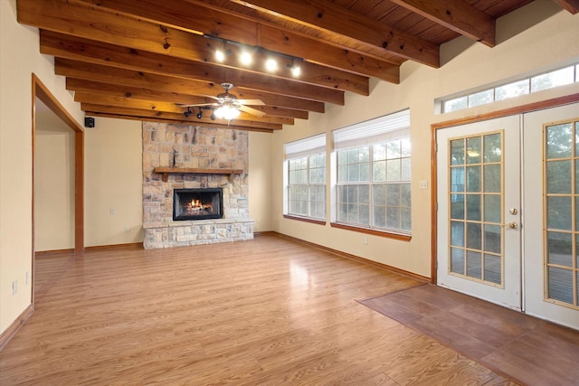 unfurnished living room featuring a ceiling fan, french doors, a stone fireplace, and wood finished floors