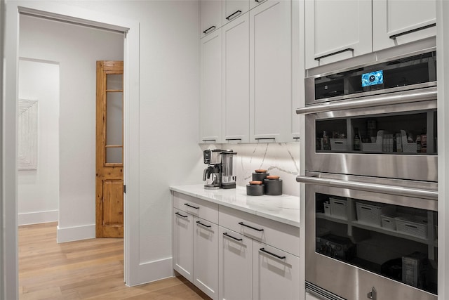 kitchen featuring light stone countertops, baseboards, double oven, light wood finished floors, and white cabinetry