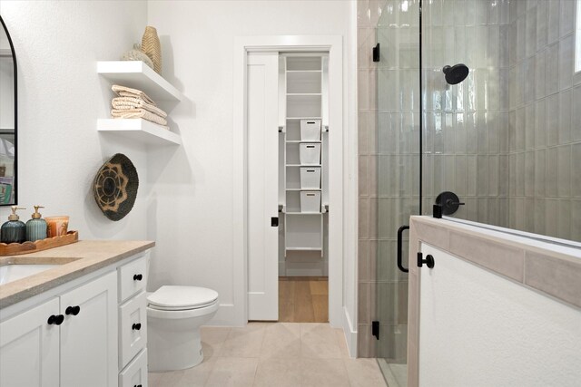 full bath with a walk in closet, tile patterned flooring, a stall shower, vanity, and toilet