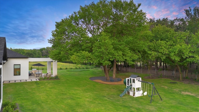 yard at dusk featuring a playground, fence, and a patio