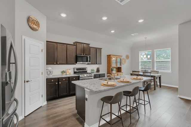 kitchen with wood finished floors, dark brown cabinetry, a kitchen breakfast bar, a sink, and stainless steel appliances