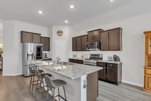 kitchen featuring stainless steel appliances, dark brown cabinetry, a sink, and light wood finished floors