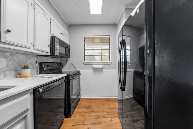 kitchen featuring white cabinets, a textured ceiling, a wainscoted wall, light wood-type flooring, and black appliances