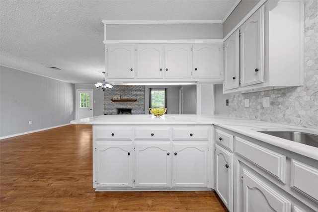 kitchen with a textured ceiling, a peninsula, wood finished floors, and white cabinetry