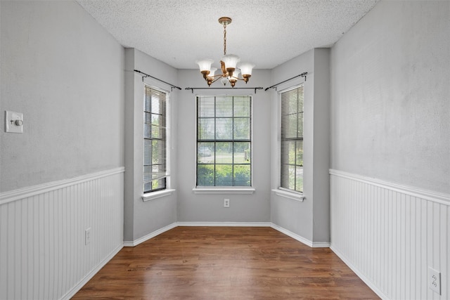 unfurnished dining area featuring an inviting chandelier, a textured ceiling, wood finished floors, and a healthy amount of sunlight