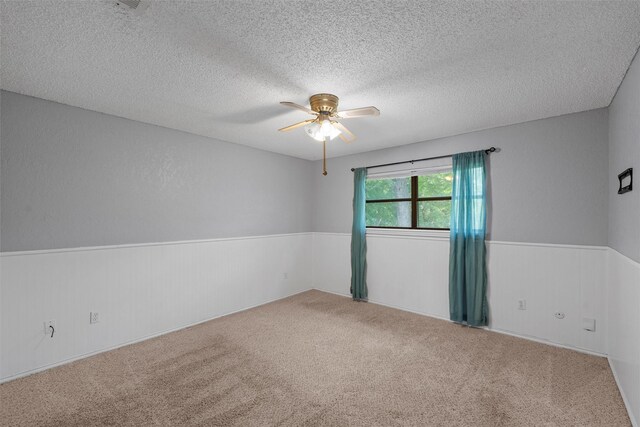 empty room featuring carpet floors, a ceiling fan, wainscoting, and a textured ceiling