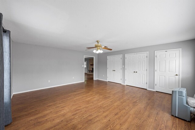 unfurnished bedroom featuring baseboards, a ceiling fan, two closets, and wood finished floors