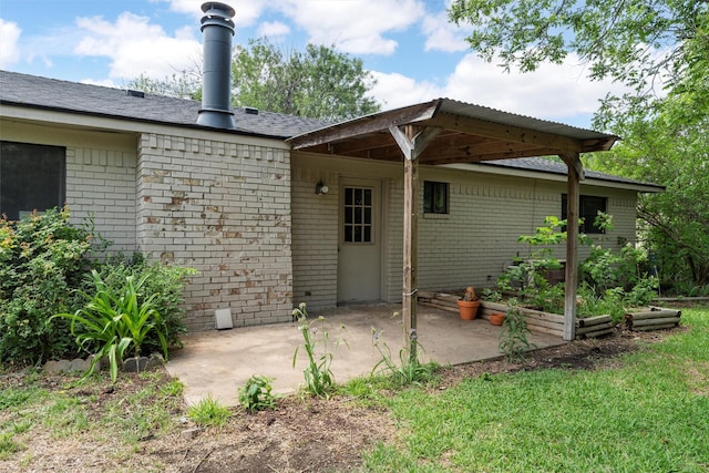 back of property with a garden, a patio, roof with shingles, brick siding, and a lawn