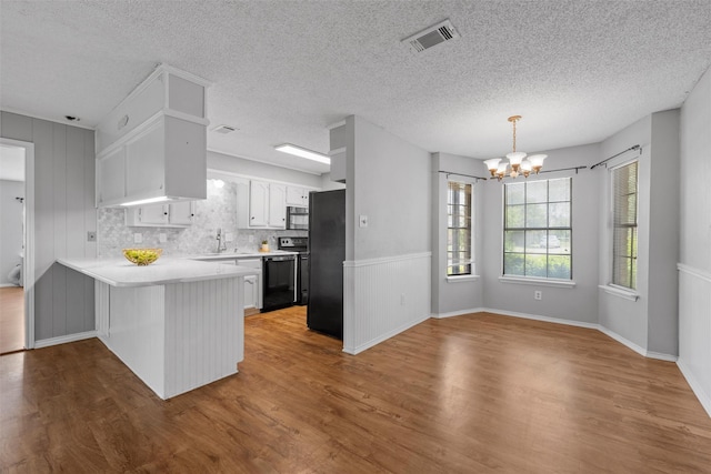 kitchen featuring wood finished floors, a peninsula, a notable chandelier, and black appliances