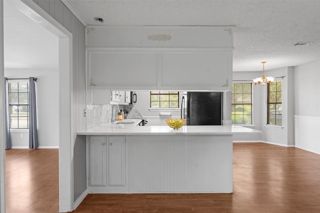 kitchen featuring an inviting chandelier, black fridge, a sink, dark wood finished floors, and a peninsula