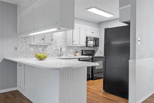 kitchen with a sink, a peninsula, wood finished floors, and black appliances