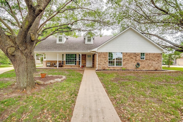 new england style home featuring covered porch, a shingled roof, and brick siding
