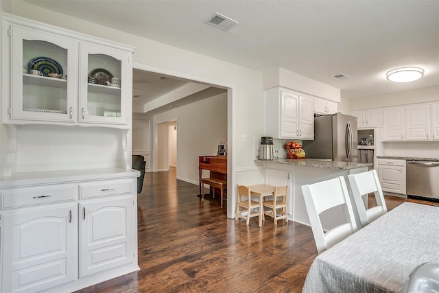 kitchen featuring visible vents, a breakfast bar, glass insert cabinets, white cabinets, and stainless steel appliances