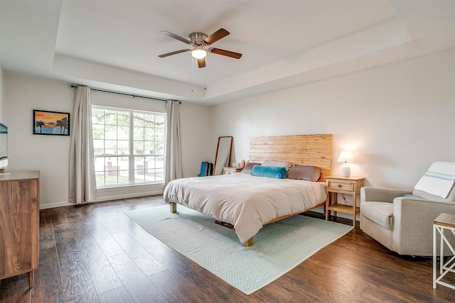 bedroom featuring dark wood-type flooring, a ceiling fan, a raised ceiling, and baseboards