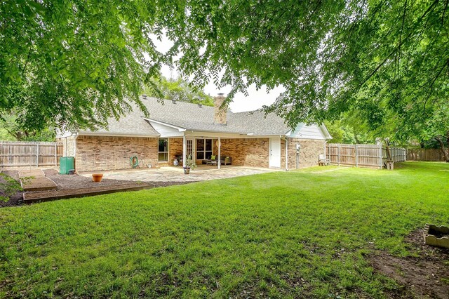 back of house with a chimney, roof with shingles, a lawn, a fenced backyard, and a patio