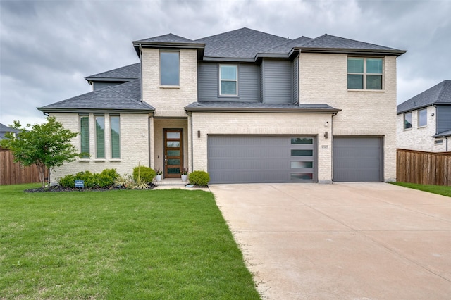 prairie-style house with a front lawn, fence, a shingled roof, an attached garage, and driveway