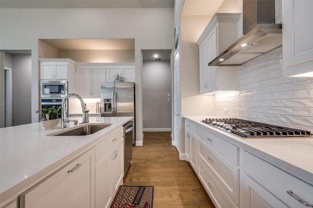 kitchen with wall chimney range hood, white cabinetry, tasteful backsplash, a sink, and stainless steel appliances