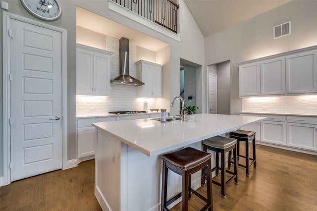 kitchen featuring visible vents, a sink, wall chimney range hood, and tasteful backsplash