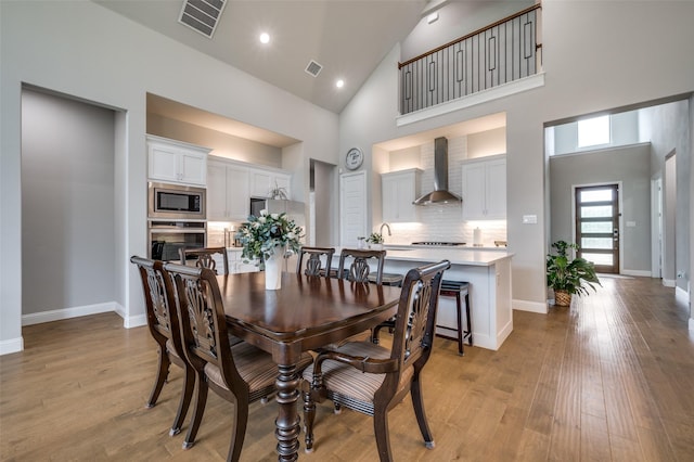 dining area featuring visible vents, light wood-style floors, baseboards, and high vaulted ceiling