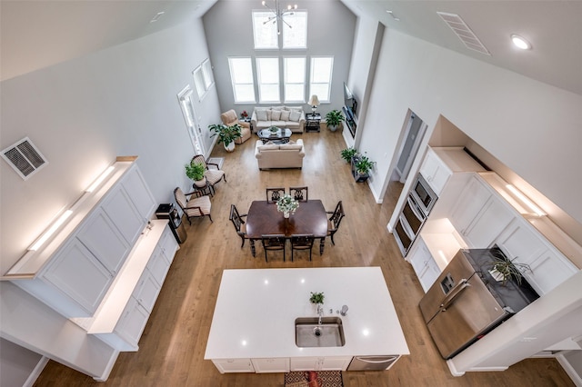 living room with high vaulted ceiling, visible vents, an inviting chandelier, and light wood finished floors