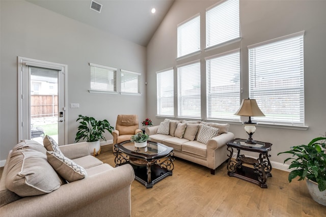 living area with high vaulted ceiling, plenty of natural light, baseboards, and visible vents