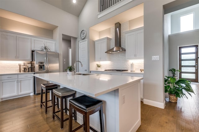 kitchen featuring appliances with stainless steel finishes, a sink, high vaulted ceiling, wall chimney exhaust hood, and decorative backsplash