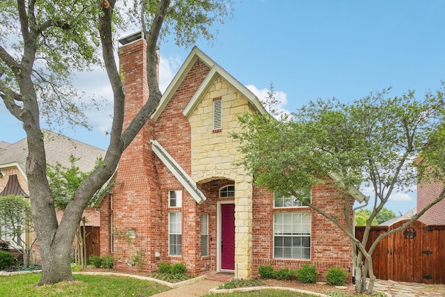 tudor home featuring fence, a gate, a chimney, and brick siding