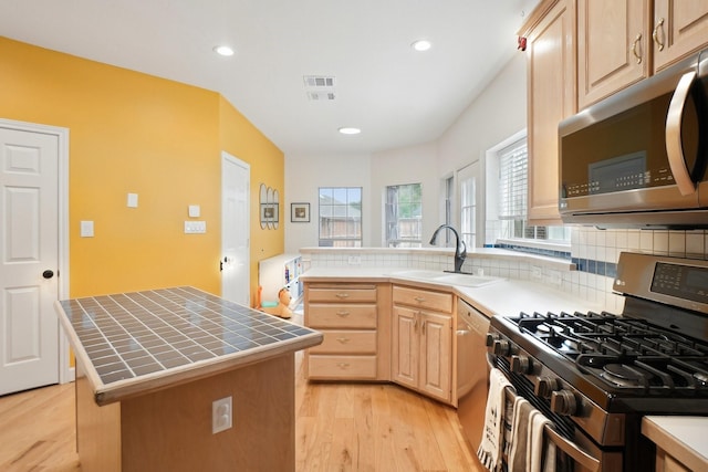 kitchen featuring light brown cabinetry, light wood-type flooring, a sink, tile counters, and stainless steel appliances