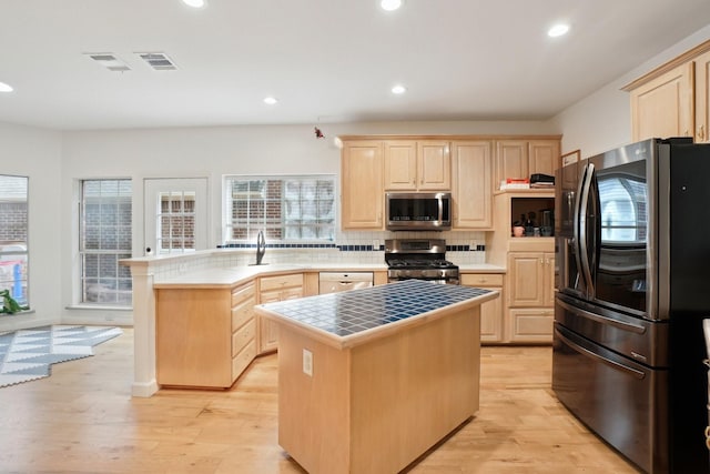 kitchen featuring light brown cabinetry, appliances with stainless steel finishes, a sink, tile counters, and decorative backsplash