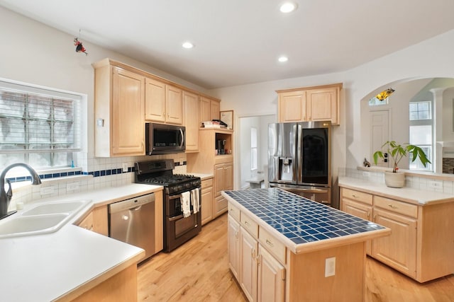 kitchen with light brown cabinetry, appliances with stainless steel finishes, arched walkways, and a sink