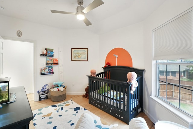 bedroom featuring a crib, baseboards, a ceiling fan, and wood finished floors