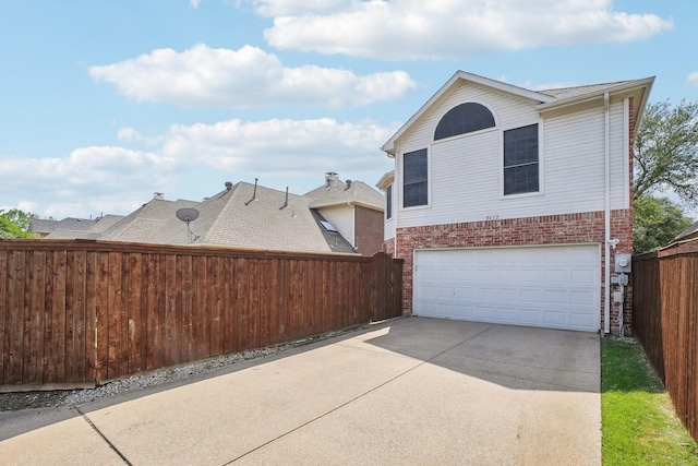 view of side of home featuring fence, an attached garage, concrete driveway, and brick siding