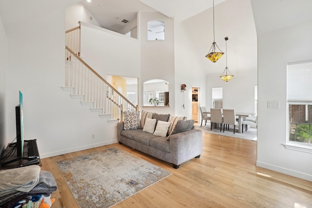 living room with arched walkways, light wood-type flooring, stairway, high vaulted ceiling, and baseboards