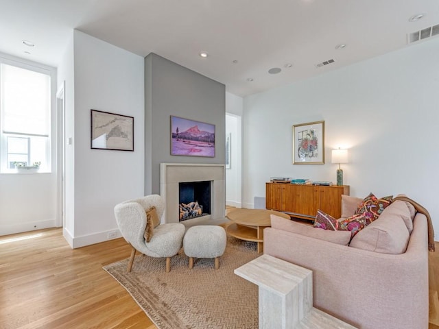living area featuring baseboards, a fireplace, light wood-type flooring, and visible vents