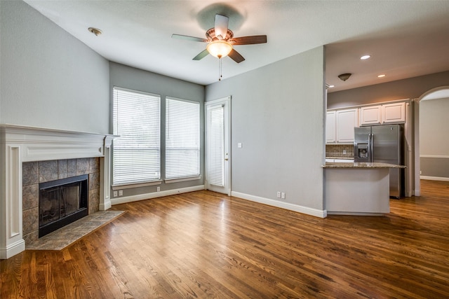 unfurnished living room with dark wood-style flooring, a ceiling fan, baseboards, and a tile fireplace