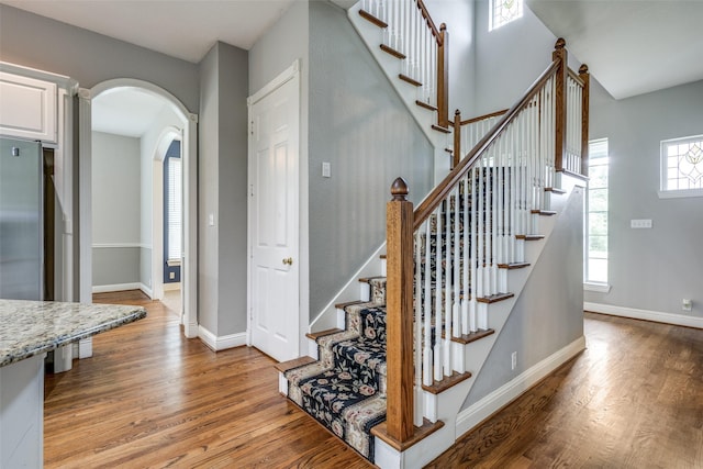 stairs featuring baseboards, arched walkways, and wood finished floors