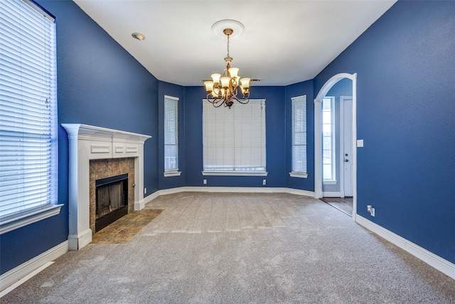 unfurnished living room with carpet floors, a chandelier, a tiled fireplace, and a healthy amount of sunlight