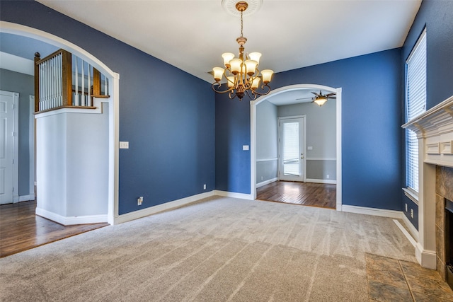 interior space featuring arched walkways, a tile fireplace, baseboards, ceiling fan with notable chandelier, and carpet flooring