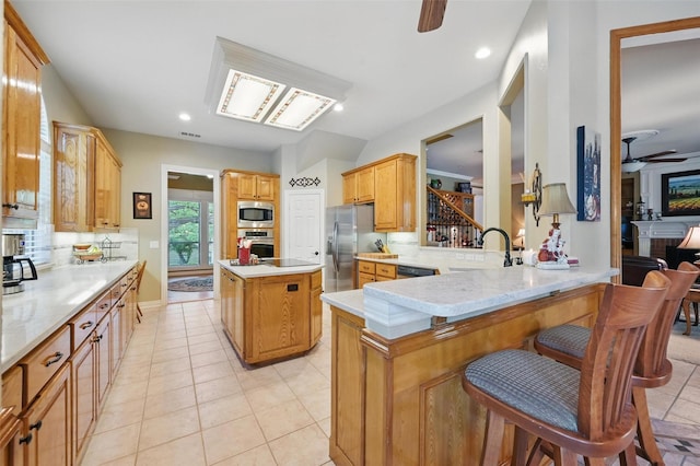 kitchen with a sink, a breakfast bar, a ceiling fan, light tile patterned floors, and stainless steel appliances