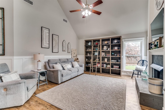 living room with a ceiling fan, visible vents, wood finished floors, high vaulted ceiling, and a wainscoted wall
