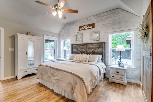 bedroom featuring wooden walls, light wood-style floors, a ceiling fan, baseboards, and lofted ceiling