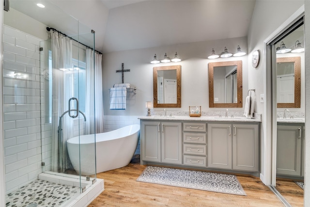 full bathroom featuring double vanity, a shower stall, wood finished floors, a sink, and a soaking tub