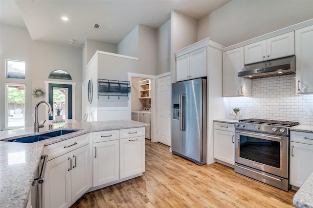 kitchen with appliances with stainless steel finishes, a sink, decorative backsplash, under cabinet range hood, and washing machine and dryer