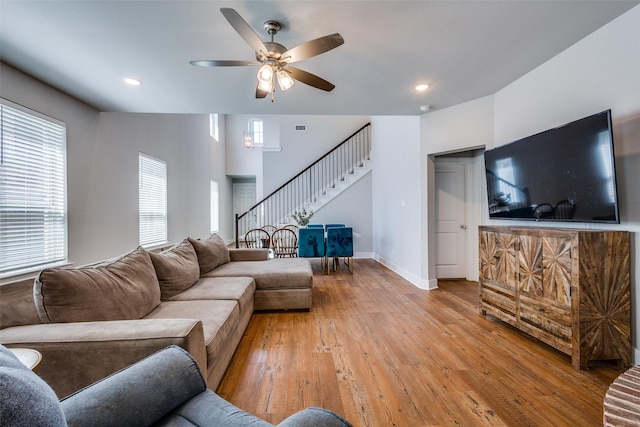 living area featuring ceiling fan, light wood finished floors, baseboards, visible vents, and stairway